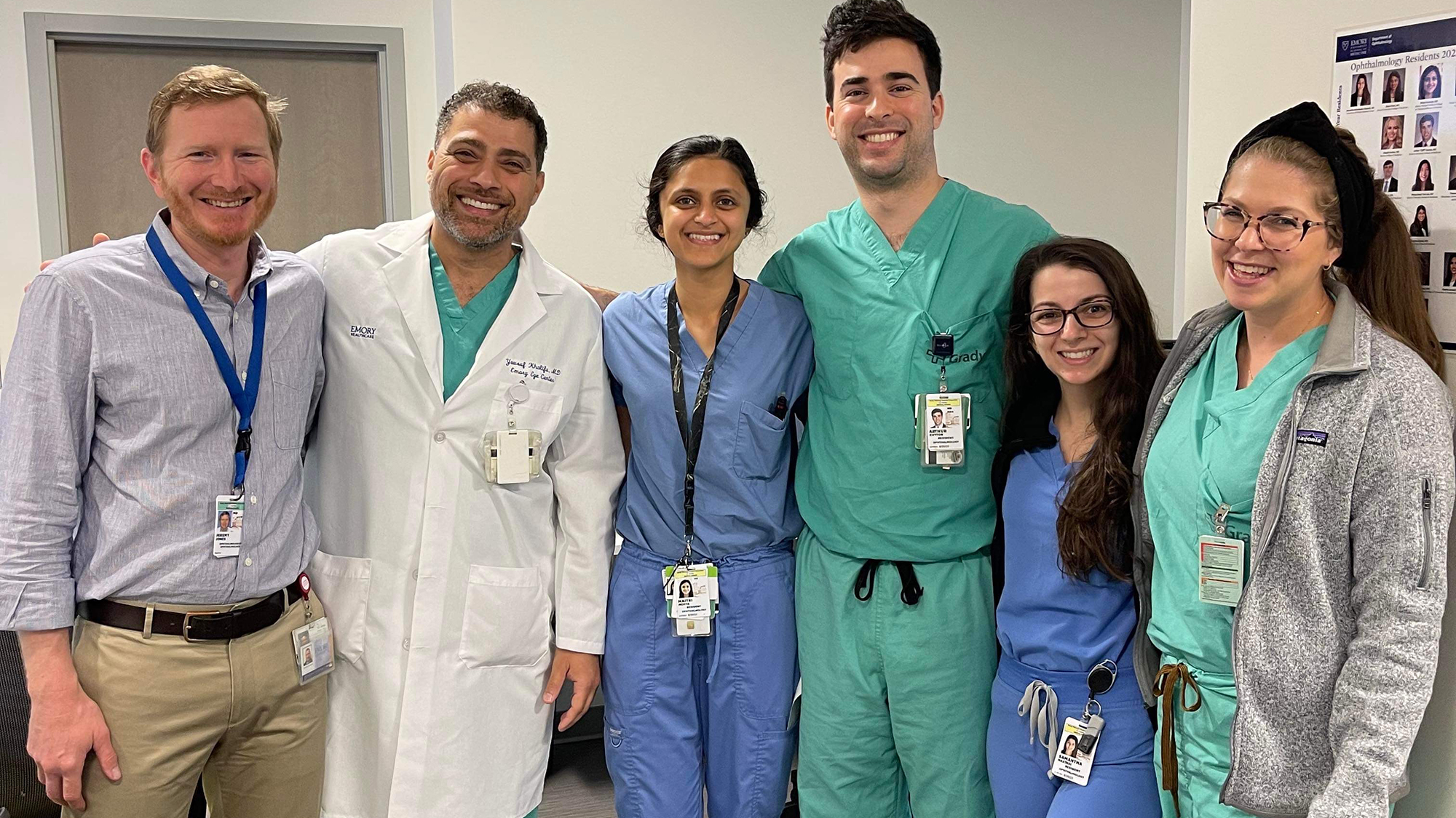 a group photo of faculty clinicians and fourth-year residents arm-in-arm after exiting from surgery for the day