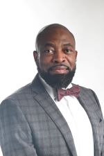 man with full black beard and shaved head wearing a grey and burgundy windowpane checked sport coat over a white shirt and burgundy bowtie